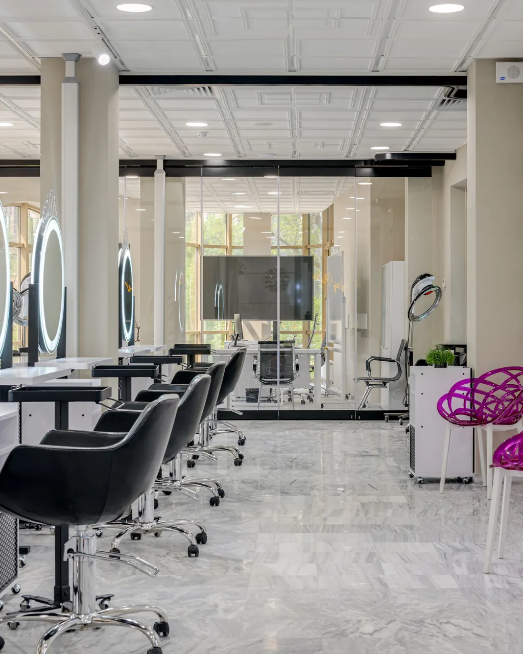 Salon de coiffure lumineux : miroirs ronds éclairés et fauteuils noirs sur sol en marbre.