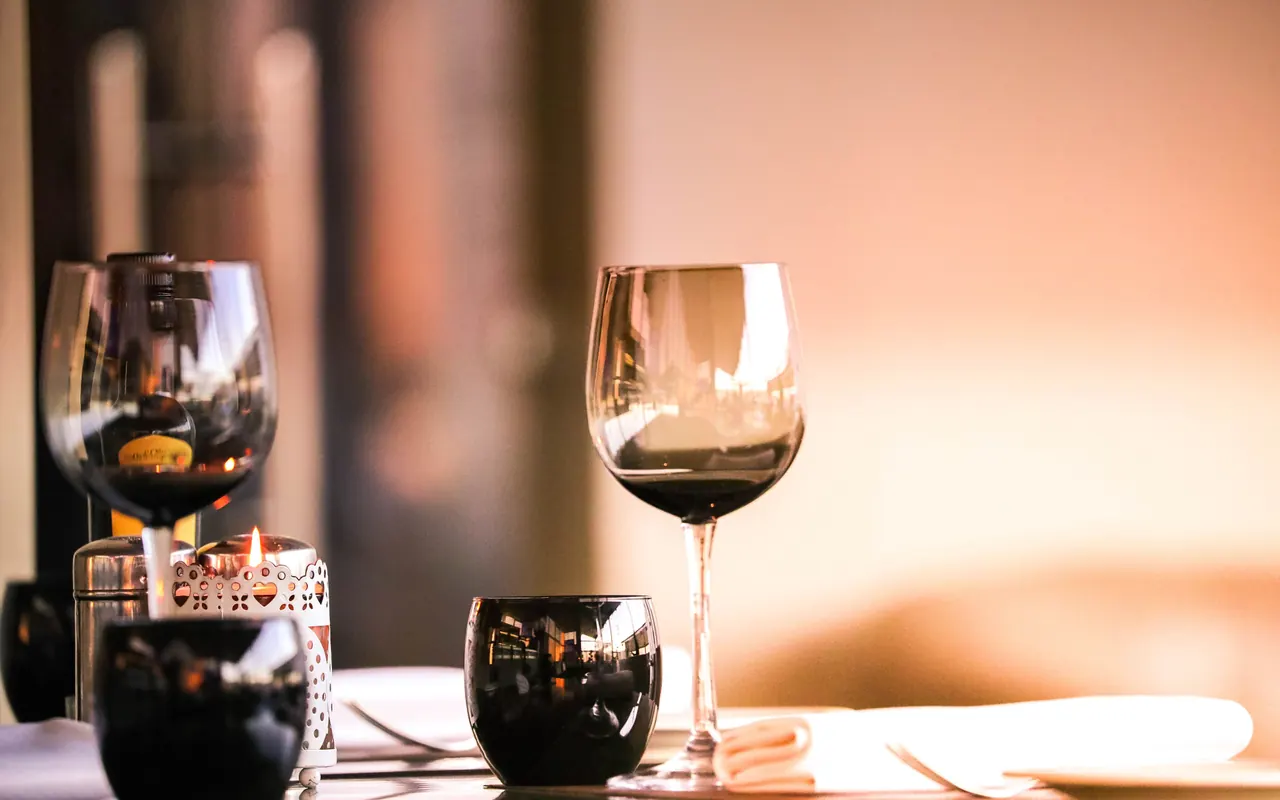Verres de vin sur une table dressée, près d'une bougie, dans la lumière du soir.